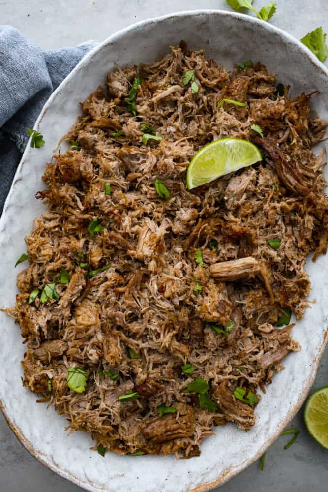 Making carnitas in an Instant Pot is foolproof. With just a few simple ingredients and the magic of pressure cooking, you can have a delicious and satisfying meal ready in no time. Make a batch of this juicy shredded pork for your next taco night, you won't regret it! Top-down view of carnitas in a large serving dish, garnished with a lime slice.