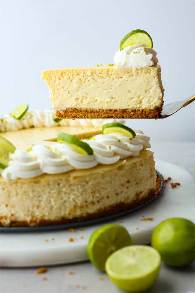 Experience the perfect summer treat with this key lime cheesecake. Made with a scrumptious graham cracker crust and topped with lime zest whipped cream, this creamy but juicy dessert is a refreshing delight! Each bite is the perfect combination of tart and sweet. A slice of key lime cheesecake being served with a metal cake spatula.