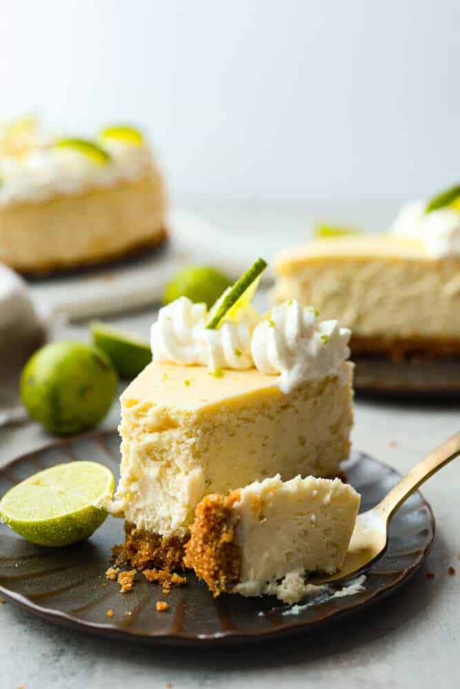Experience the perfect summer treat with this key lime cheesecake. Made with a scrumptious graham cracker crust and topped with lime zest whipped cream, this creamy but juicy dessert is a refreshing delight! Each bite is the perfect combination of tart and sweet. Hero image of key lime cheesecake slice with a bite taken out of it.