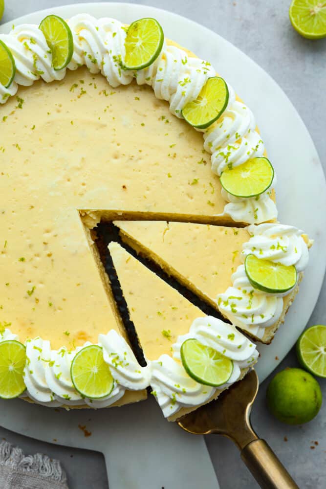 Experience the perfect summer treat with this key lime cheesecake. Made with a scrumptious graham cracker crust and topped with lime zest whipped cream, this creamy but juicy dessert is a refreshing delight! Each bite is the perfect combination of tart and sweet. Top-down view of cheesecake, cut into slices.