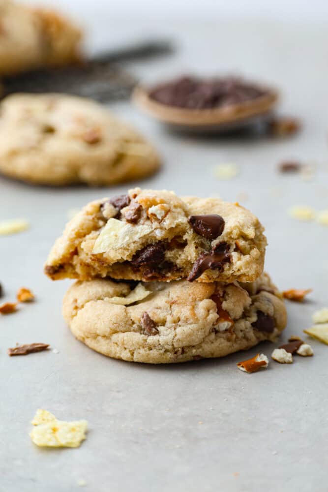 These kitchen sink cookies are the perfect chaotic blend of pretty much everything but the kitchen sink! A chocolate chip cookie is taken to the next level with pretzels, potato chips, and candy pieces. You won't be able to get over how amazing these cookies are! A kitchen sink cookie broken in half stacked on top of each other.