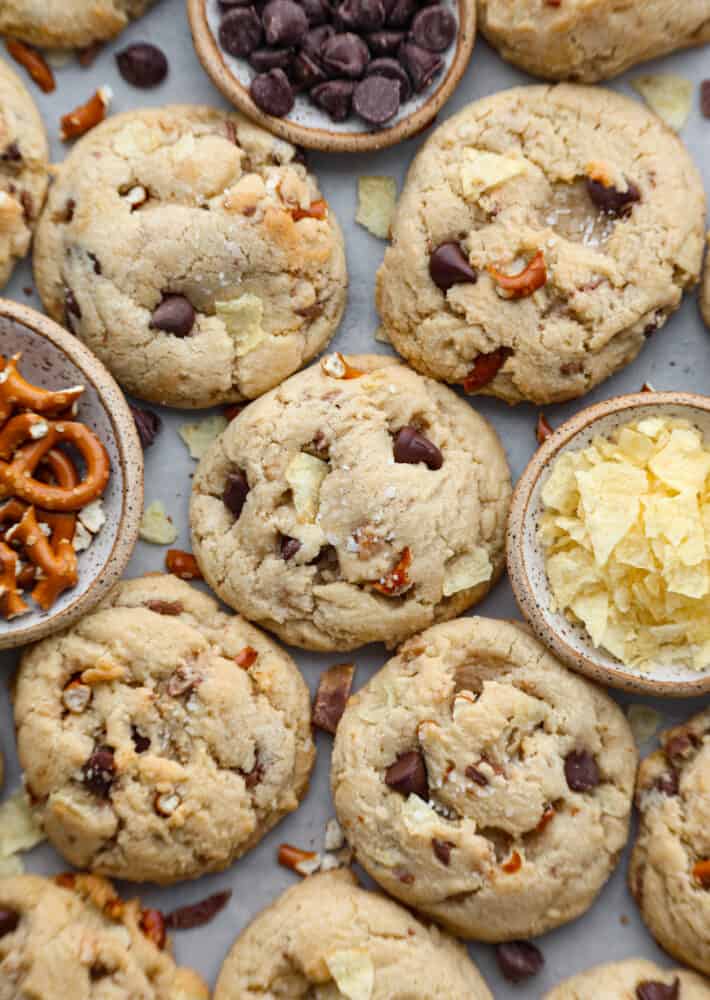 These kitchen sink cookies are the perfect chaotic blend of pretty much everything but the kitchen sink! A chocolate chip cookie is taken to the next level with pretzels, potato chips, and candy pieces. You won't be able to get over how amazing these cookies are! Kitchen sink cookies with extra ingredients surrounding them.