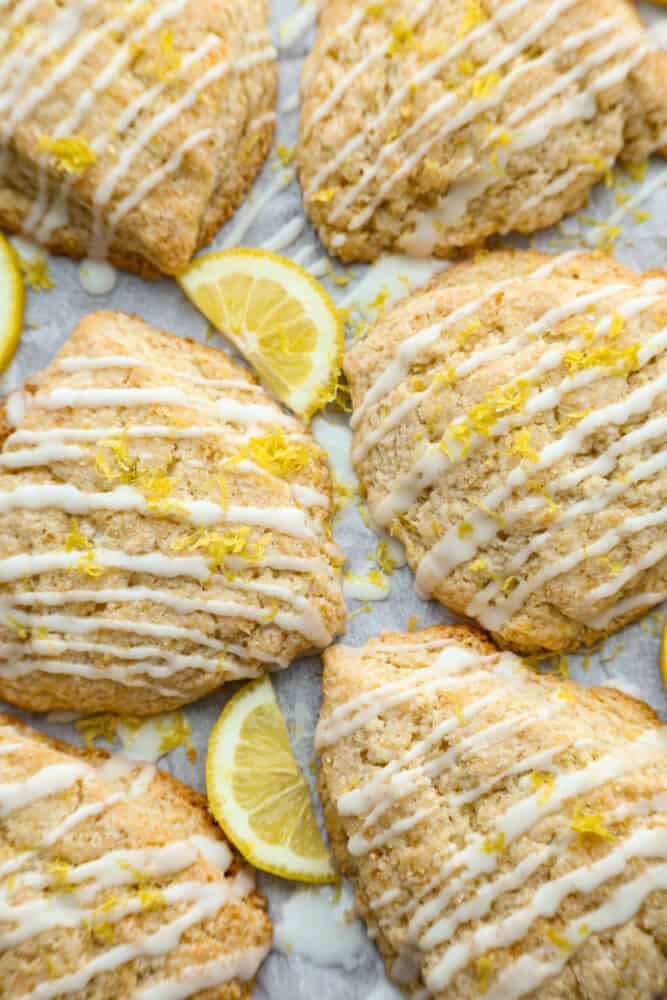 These homemade lemon scones are the perfect balance of tangy and sweet, with a crumbly texture that'll melt in your mouth. And let's not forget about the delicious sweet lemon icing, which is the cherry on top to make them simply irresistible. Having one of these for breakfast is the perfect way to start your day! Multiple scones drizzled with icing on a baking sheet.
