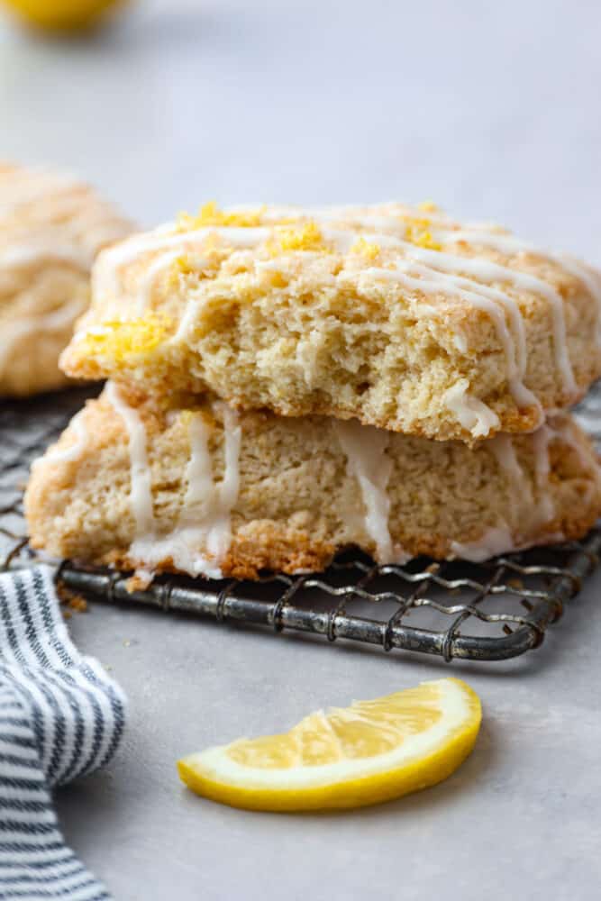 These homemade lemon scones are the perfect balance of tangy and sweet, with a crumbly texture that'll melt in your mouth. And let's not forget about the delicious sweet lemon icing, which is the cherry on top to make them simply irresistible. Having one of these for breakfast is the perfect way to start your day! 2 lemon scones stacked on top of each other.