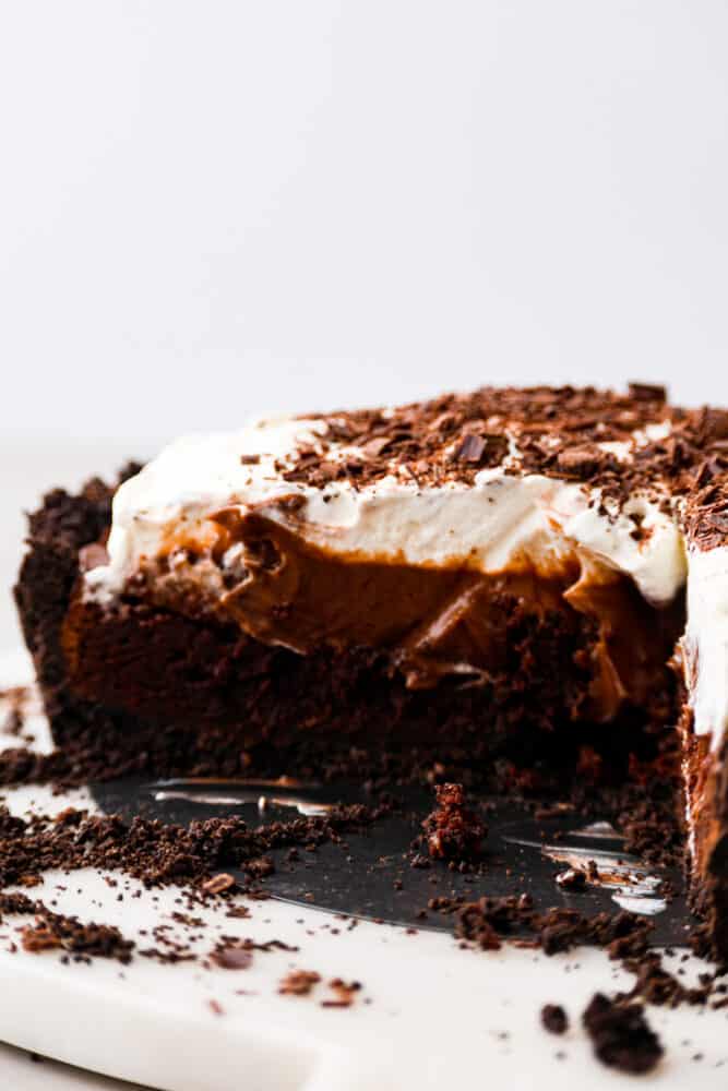 Chocolate lovers, this Mississippi Mud Pie is for you! A silky chocolate filling topped with whipped cream and chocolate shavings, all eaten on an Oreo crust. It doesn't get much more delicious than that! The side view of a Mississippi mud pie with a slice cute out so that you can see the inside layers of the pie.