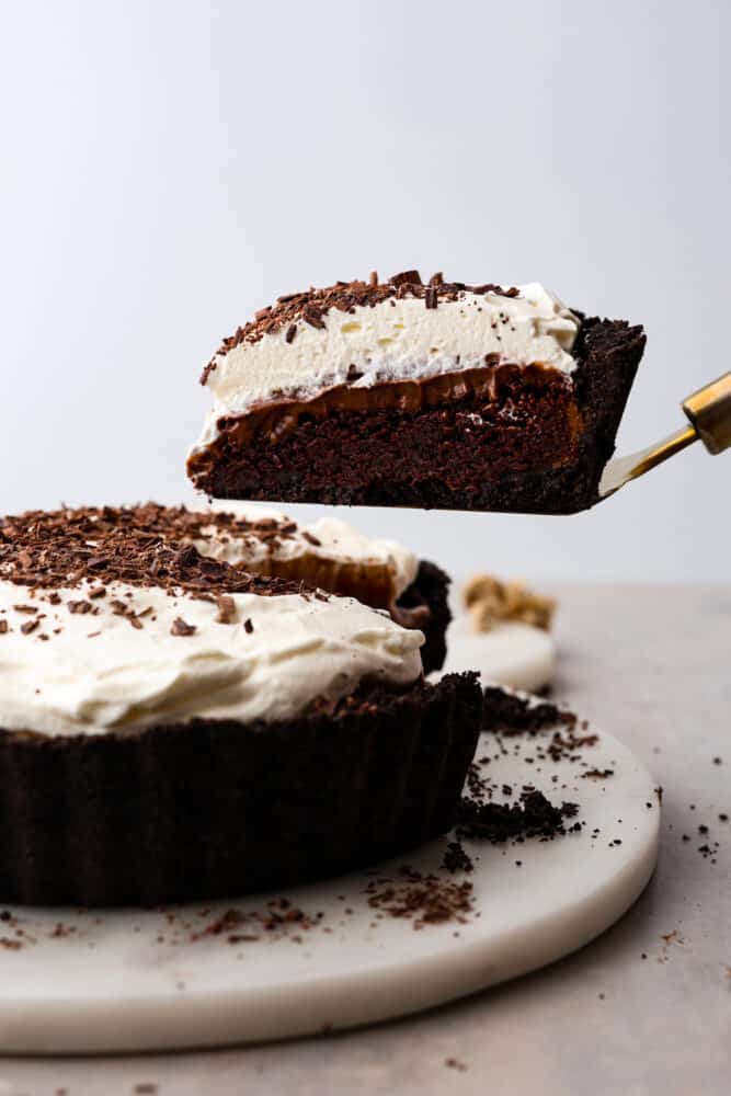 Chocolate lovers, this Mississippi Mud Pie is for you! A silky chocolate filling topped with whipped cream and chocolate shavings, all eaten on an Oreo crust. It doesn't get much more delicious than that! A slice of Mississippi mud pie being taken out with a gold server.