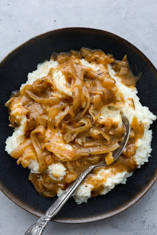 This onion gravy is hands-down the BEST! It's rich, savory and filled with sweet, caramelized onions that really take it to the next level. Gravy served over mashed potatoes in a black dish.