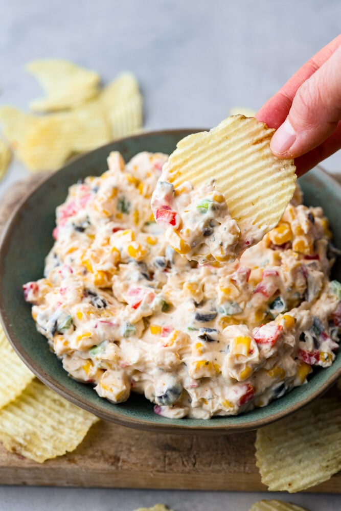 Loaded Creamy Ranch Dip is packed with so many delicious flavors that friends and family won't be able to get enough of it. Perfect for the pool or potlucks! A bowl of poolside dip with a potato chip scooping some dip.