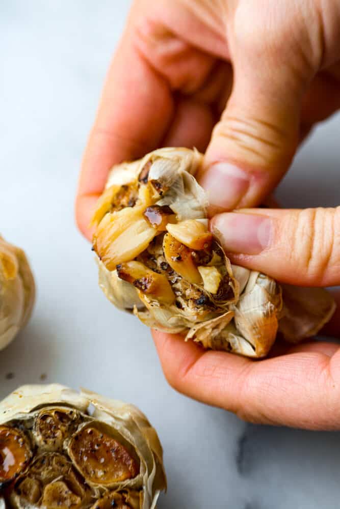 If you want to infuse your favorite recipes with savory, nutty flavor, roasted garlic is the way to go! You can easily make some at home in a muffin tin with a drizzle of olive oil on top to enhance the overall flavor! The end result is caramelized, garlic heaven. A garlic head being torn open to reveal the cloves inside.