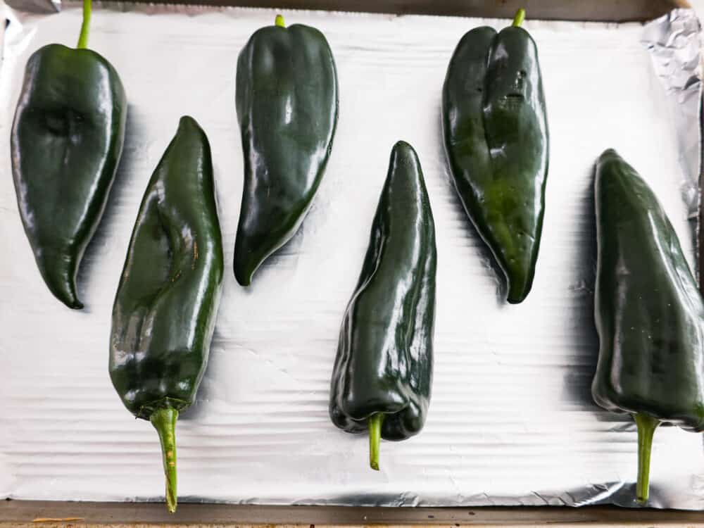 If you're a fan of peppers and haven't tried roasted poblano peppers yet, you're missing out! These peppers have a unique flavor that is smoky, slightly sweet, and just a little bit spicy. Roasting them brings out their full potential, making them perfect for giving your favorite Mexican dishes a little kick. Lining up peppers on a baking sheet.