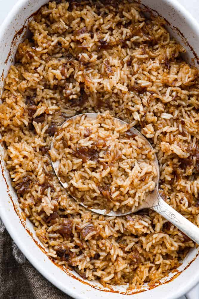 Stick of Butter Baked Rice is soft and fluffy rice that is loaded with sweet, rich flavors from onion soup and butter.ย It is quick and easy to prep and bakes in the oven to perfection! A close up of baked rice in a casserole dish.