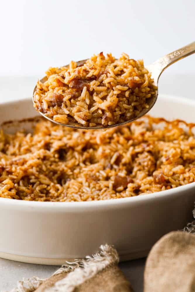 Stick of Butter Baked Rice is soft and fluffy rice that is loaded with sweet, rich flavors from onion soup and butter.ย It is quick and easy to prep and bakes in the oven to perfection! A gold spoon scooping up baked rice from a casserole dish.
