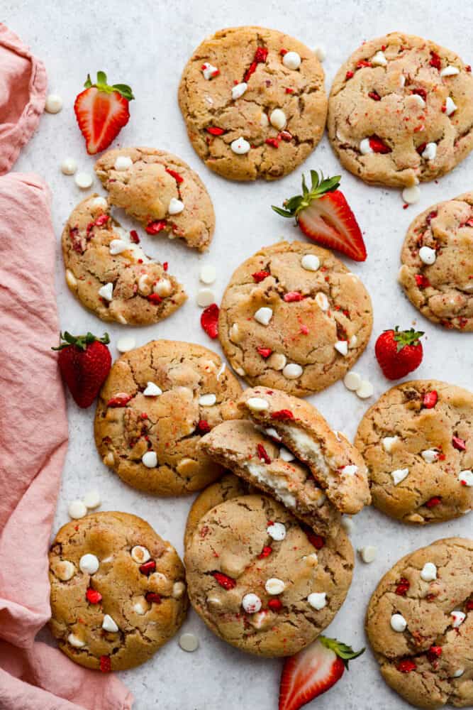 Meet your new favorite cookie recipe: soft and sweet strawberry cookies filled with a gooey cheesecake center. These golden-brown morsels of goodness will be devoured as soon as theyโre out of the oven! Top-down view of strawberry cheesecake cookies, with some of them broken in half.