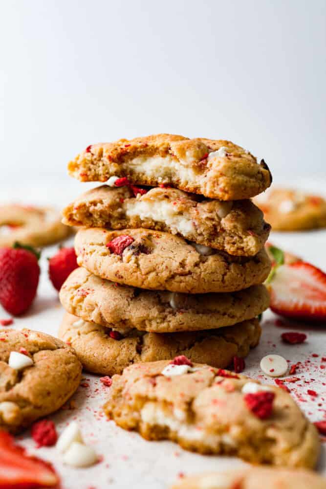 Meet your new favorite cookie recipe: soft and sweet strawberry cookies filled with a gooey cheesecake center. These golden-brown morsels of goodness will be devoured as soon as theyโre out of the oven! 5 cookies stacked on top of each other. One is broken in half so the cheesecake filling can be seen.