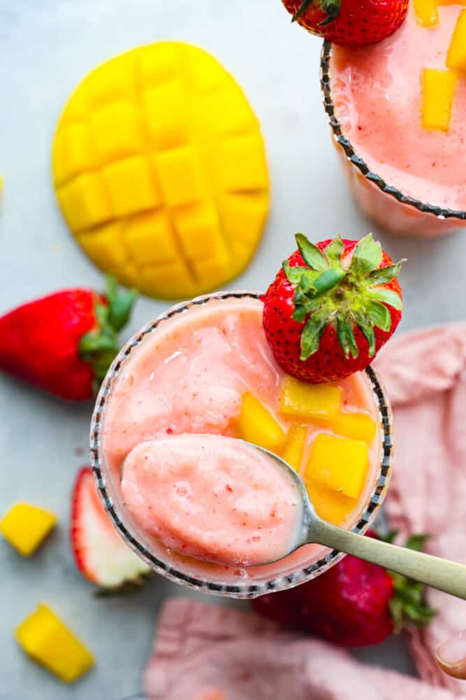This delightful Strawberry Mango Smoothie recipe is a burst of tropical flavors that will transport you to paradise. With just a handful of ingredients and a blender, you'll be sipping on this refreshing treat in no time. The top view of a glass with strawberry mango smoothie in it and a spoon scooping some out.