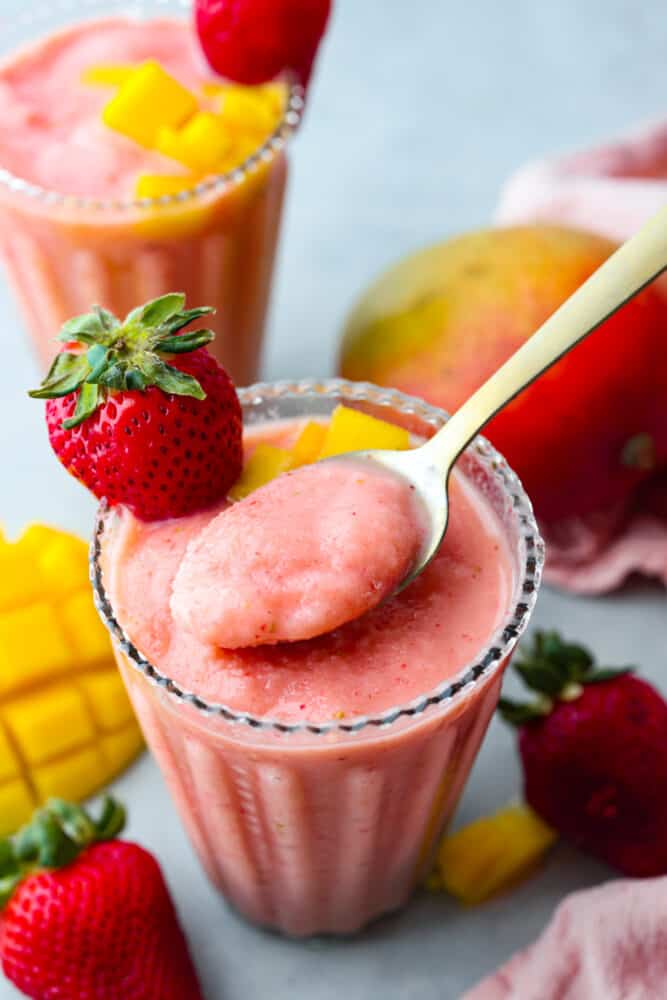 This delightful Strawberry Mango Smoothie recipe is a burst of tropical flavors that will transport you to paradise. With just a handful of ingredients and a blender, you'll be sipping on this refreshing treat in no time. A close up of a spoon in a glass filled with strawberry mango smoothie.