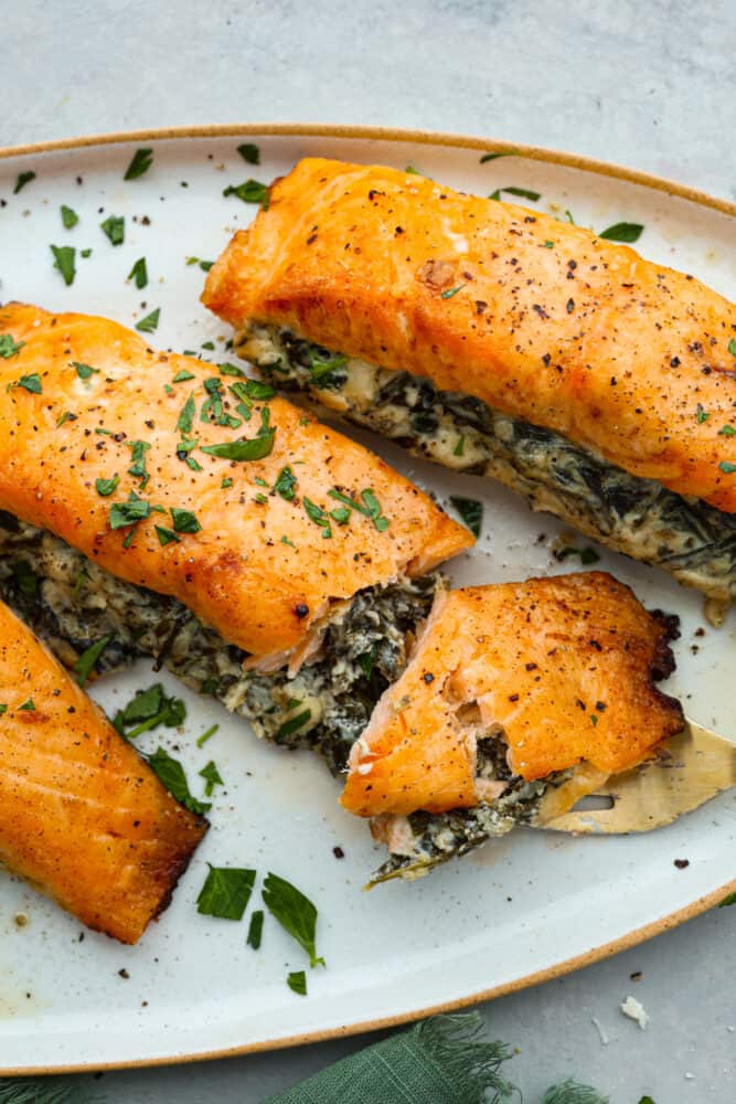 This spinach stuffed salmon is a flavor explosion, with the creamy richness of the cheese and the earthy goodness of the spinach perfectly complementing the tender, flaky salmon. It's a restaurant-quality meal that's ready in just 45 minutes! Closeup of stuffed salmon with a bite taken out of it, so the cream cheese spinach filling can be seen.