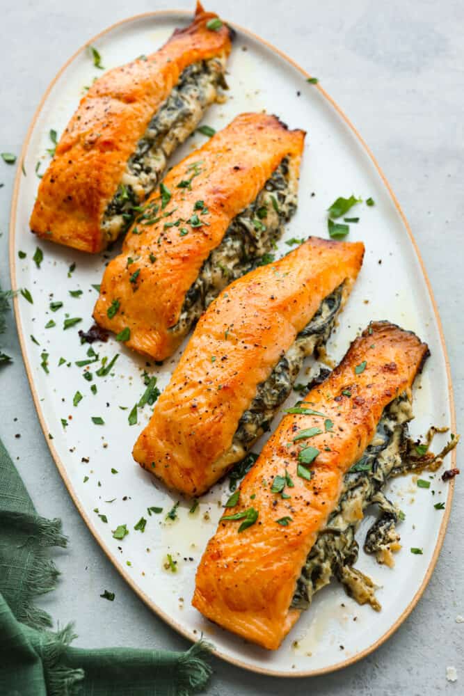 This spinach stuffed salmon is a flavor explosion, with the creamy richness of the cheese and the earthy goodness of the spinach perfectly complementing the tender, flaky salmon. It's a restaurant-quality meal that's ready in just 45 minutes! 4 pieces of cooked fish on a white plate.