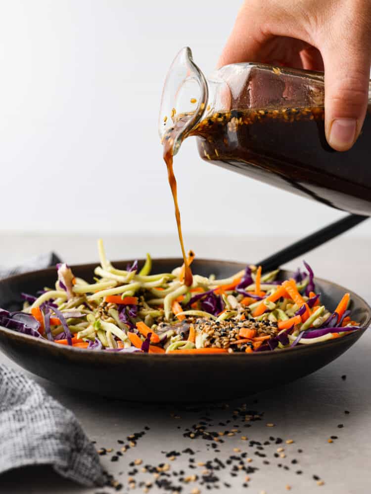 Packed with tangy, savory flavor, and sesame seeds for texture, this homemade Asian salad dressing is the perfect addition to your favorite bowl of greens. It’s made without preservatives and artificial flavors for a dressing you can feel great about using! Dressing being poured over a bowl of vegetables.