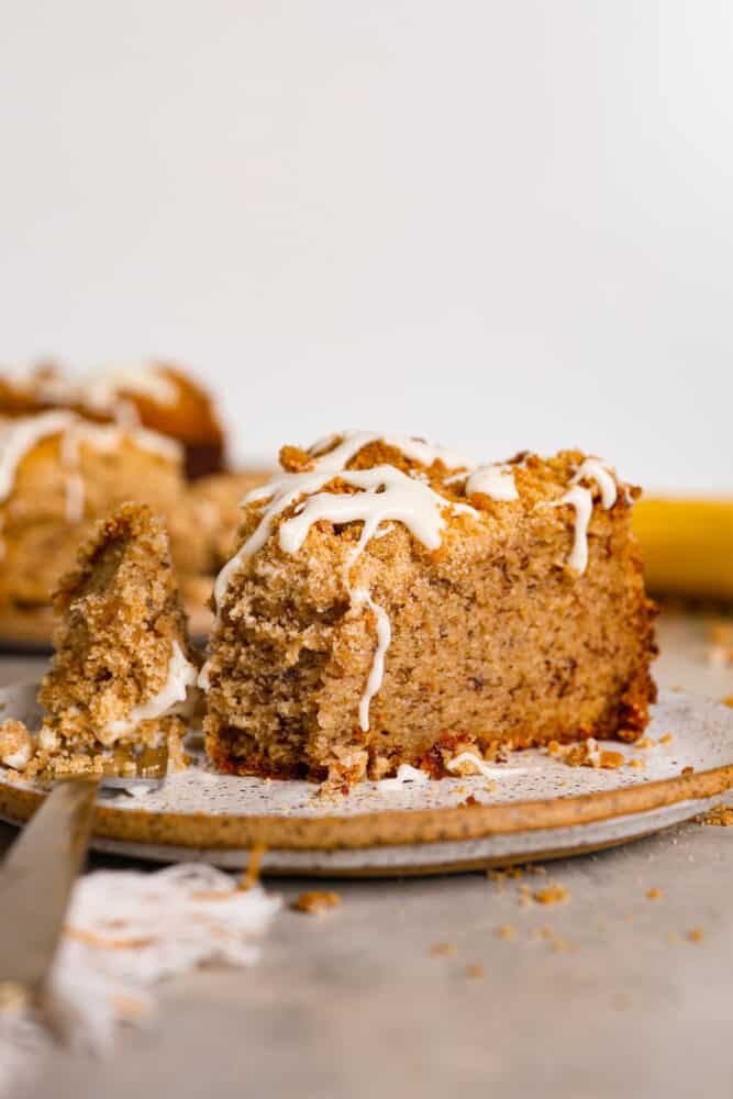 Banana coffee cake is a great way to use up any overripe bananas you might have lying around! With a moist, fluffy, vanilla banana-flavored interior and a buttery streusel topping, this is a unique twist on coffee cake that will have you hooked after the first bite! A slice of coffee cake with a bite taken out of it.