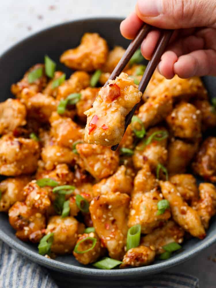 Bring a bang to your dinner table with this explosive bang bang chicken! Itโs crispy but tender and coated in a thick, creamy sauce thatโs savory, spicy, and sweet all at once! A piece of chicken being picked up with chopsticks.