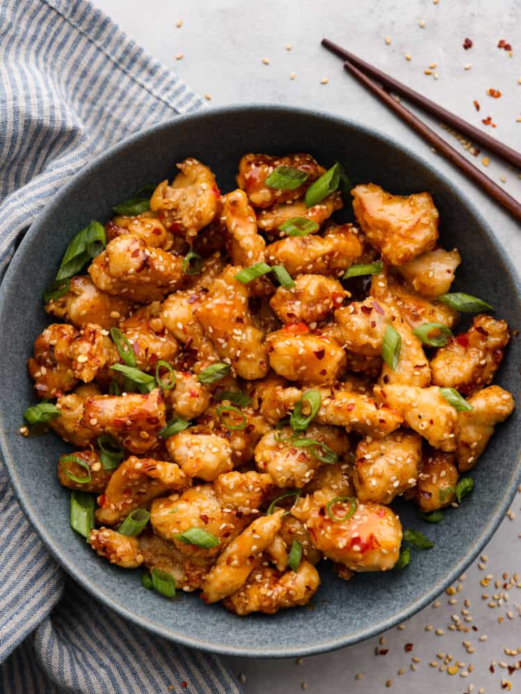 Bring a bang to your dinner table with this explosive bang bang chicken! Itโs crispy but tender and coated in a thick, creamy sauce thatโs savory, spicy, and sweet all at once! Top-down view of bang bang chicken served in a gray bowl.