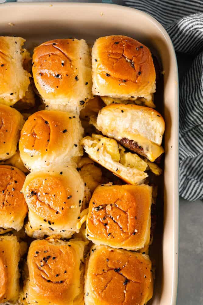 Hawaiian rolls filled with juicy sausage patties, scrambled eggs, and melty cheese, slathered in everything bagel butter. These breakfast sliders are so simple, so delicious, and perfect for feeding a crowd. Top-down view of cooked sandwiches, brushed with butter and topped with everything bagel seasoning.