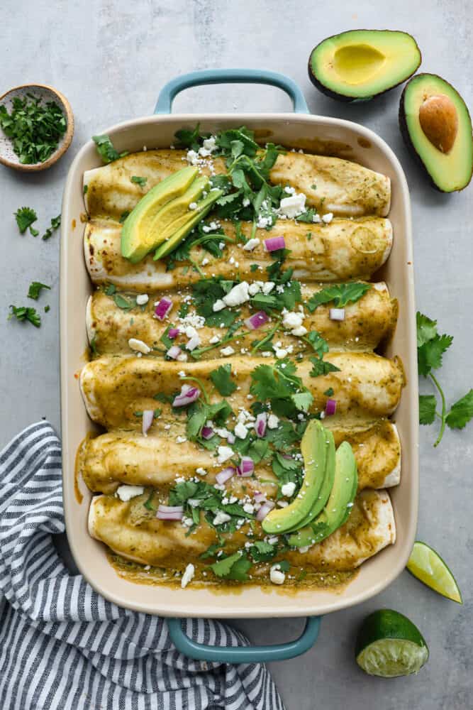 hicken Enchiladas with an Avocado Cream Sauceย is a delicious and easy weeknight meal that everyone will love. They are packed with flavor and drizzled with a sauce that dreams are made of. If you love avocados, this recipe is for you! A top view of chicken enchiladas with an avocado cream sauce in a casserole dish.