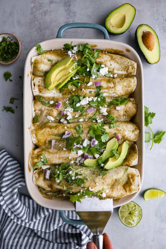 hicken Enchiladas with an Avocado Cream Sauceย is a delicious and easy weeknight meal that everyone will love. They are packed with flavor and drizzled with a sauce that dreams are made of. If you love avocados, this recipe is for you! The top few of chicken enchiladas with an avocado cream sauce in a casserole dish with a silver serve about to get an enchilada out.