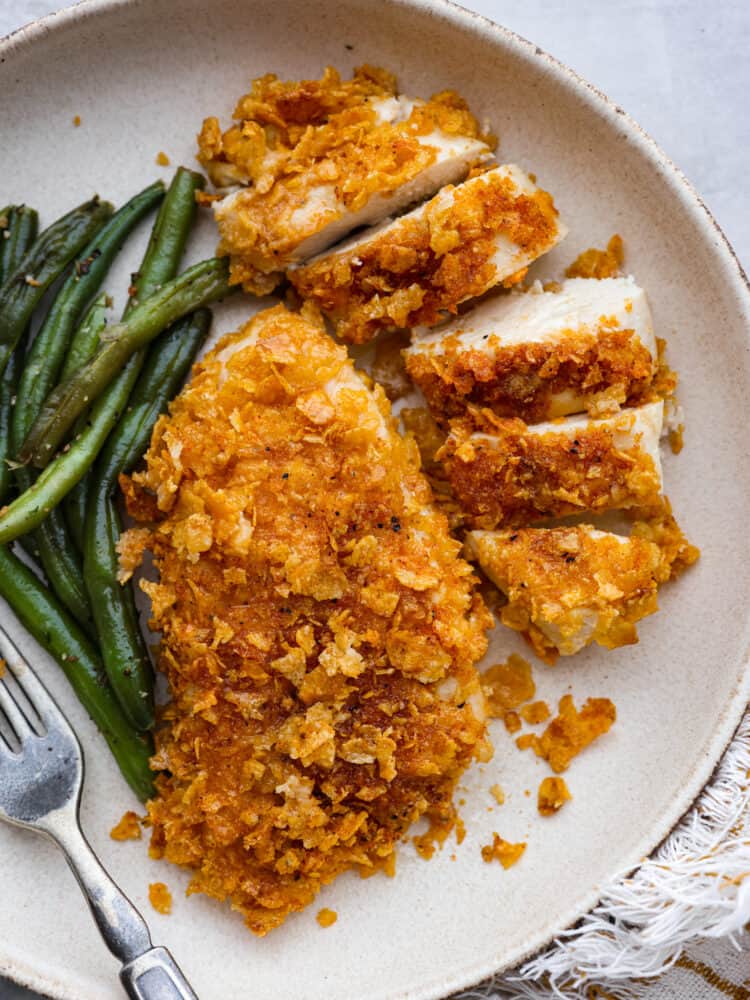 Ultra crispy-and so delicious, cornflake chicken is just the easy you dinner you need this week! Each chicken breast is coated in cornflakes and savory seasonings for both the best texture and flavor! Cornflake chicken and green beans served on a white plate.