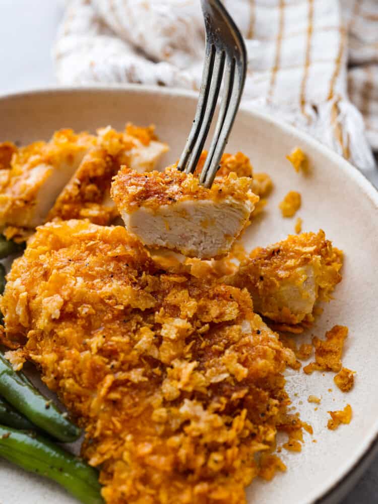 Ultra crispy-and so delicious, cornflake chicken is just the easy you dinner you need this week! Each chicken breast is coated in cornflakes and savory seasonings for both the best texture and flavor! Taking a bite of chicken with a fork.