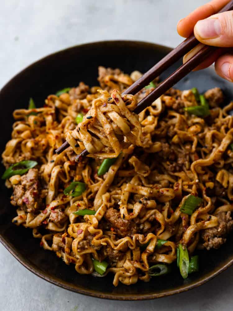 Dan Dan Noodles is a classic Chinese dish made with tender egg noodles and flavorful minced pork tossed in a savory, slightly spicy sauce. It's the perfect comfort food and will have everyone in your family wanting seconds. Picking up a bite of dan dan noodles with dark brown chopsticks.
