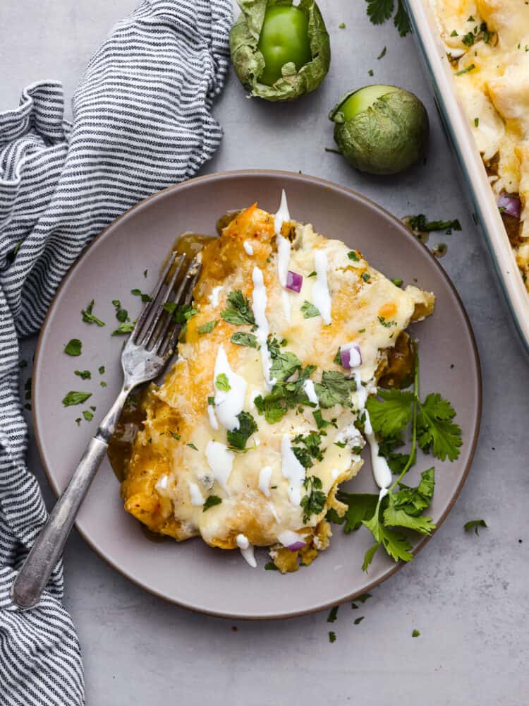 Enchiladas Suizas is a ridiculously delicious Mexican dish that'll make your taste buds go wild! Picture this: juicy shredded chicken wrapped in soft corn tortillas, slathered in a zesty tomatillo sauce, and smothered with creamy sour cream and melty cheese. Enchiladas suizas served in a gray plate.