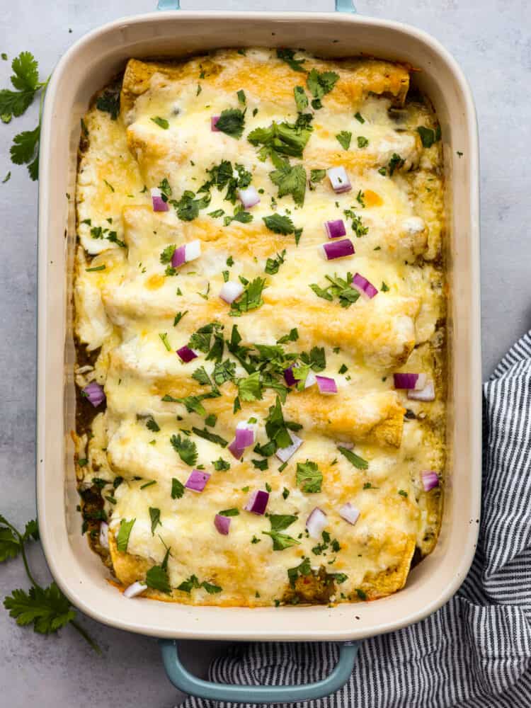 Enchiladas Suizas is a ridiculously delicious Mexican dish that'll make your taste buds go wild! Picture this: juicy shredded chicken wrapped in soft corn tortillas, slathered in a zesty tomatillo sauce, and smothered with creamy sour cream and melty cheese. Top-down view of enchiladas suizas in a baking dish.