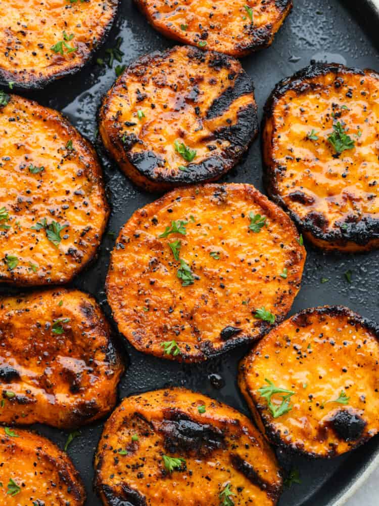 Bursting with flavor and ready in 15 minutes, these grilled sweet potatoes are a must-add to any summer barbecue lineup. Even though they're cooked to smoky perfection, each slice is nice and tender and coated in a tasty blend of savory seasonings. Closeup of grilled sweet potatoes, topped with seasonings and herbs.
