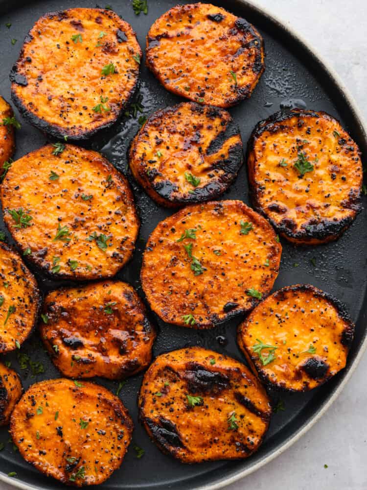 Bursting with flavor and ready in 15 minutes, these grilled sweet potatoes are a must-add to any summer barbecue lineup. Even though they're cooked to smoky perfection, each slice is nice and tender and coated in a tasty blend of savory seasonings. Grilled sweet potato slices served on a black plate.