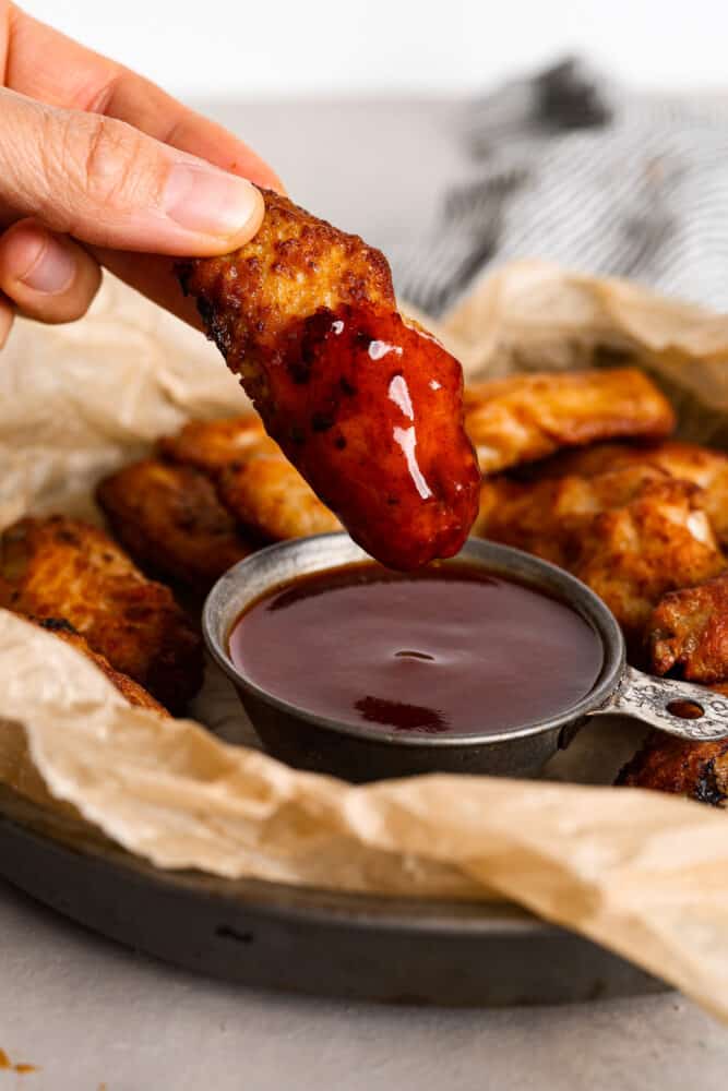 Mumbo sauce is like a dreamy combination of barbecue and sweet and sour sauce. It’s tangy and savory with a glaze-like texture that’s wonderful for coating chicken wings! Dipping a chicken wing into mumbo sauce.