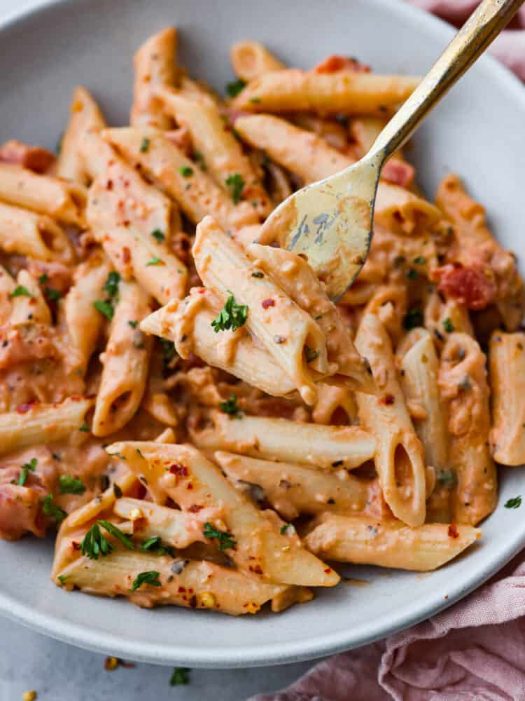 This ultra-delicious Pink Sauce Pasta recipe features penne pasta cooked al dente and tossed in a flavorful pink sauce. The dish is garnished with fresh basil and grated parmesan cheese for an extra touch of deliciousness. Pink sauce pasta one a plate with a gold fork taking a scoop out of the dish.