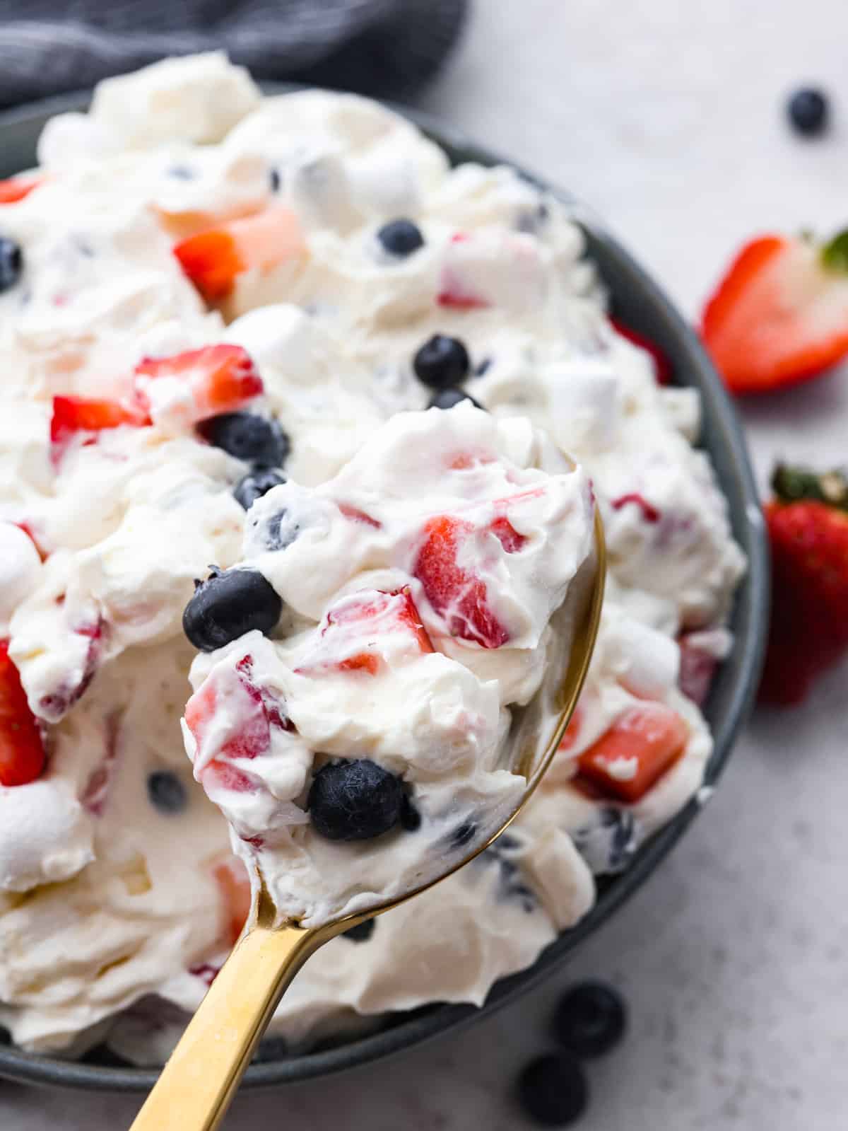 Introducing the red, white, and blue cheesecake salad, a delightful and patriotic summer fruit salad that combines the vibrant flavors of strawberries and blueberries with creamy cheesecake and fluffy marshmallows. It's super easy to throw together and a hit at every potluck! A spoonful of red white and blue cheesecake salad.