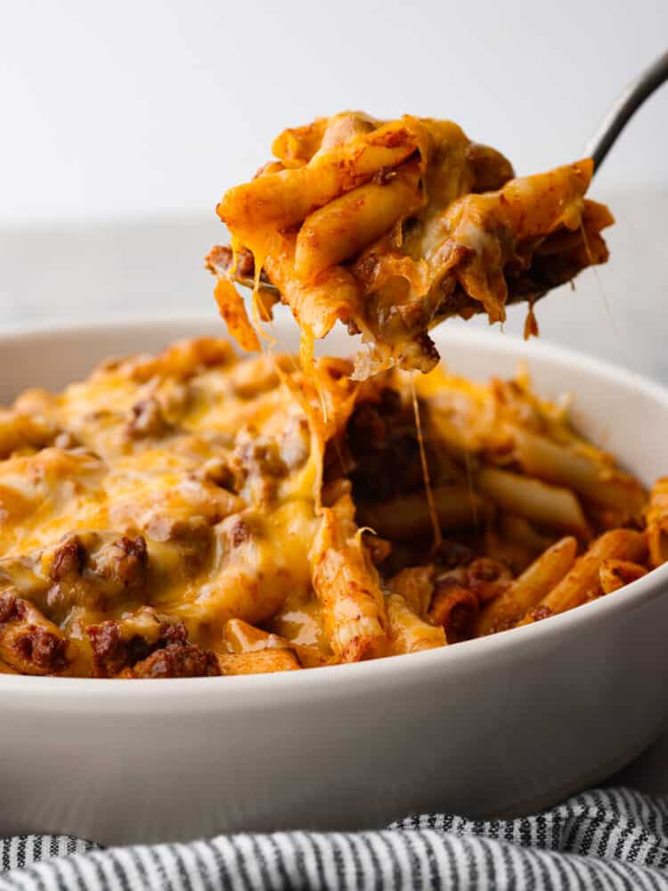 Swap out the bun for this sloppy joe casserole full of pasta and a sweet ground beef mixture. All of the meaty and delicious flavors of a sloppy joe sandwich transform into an easy weeknight meal your family will love! Close side view of sloppy jo casserole being lifted out of the baking dish with a serving spoon.