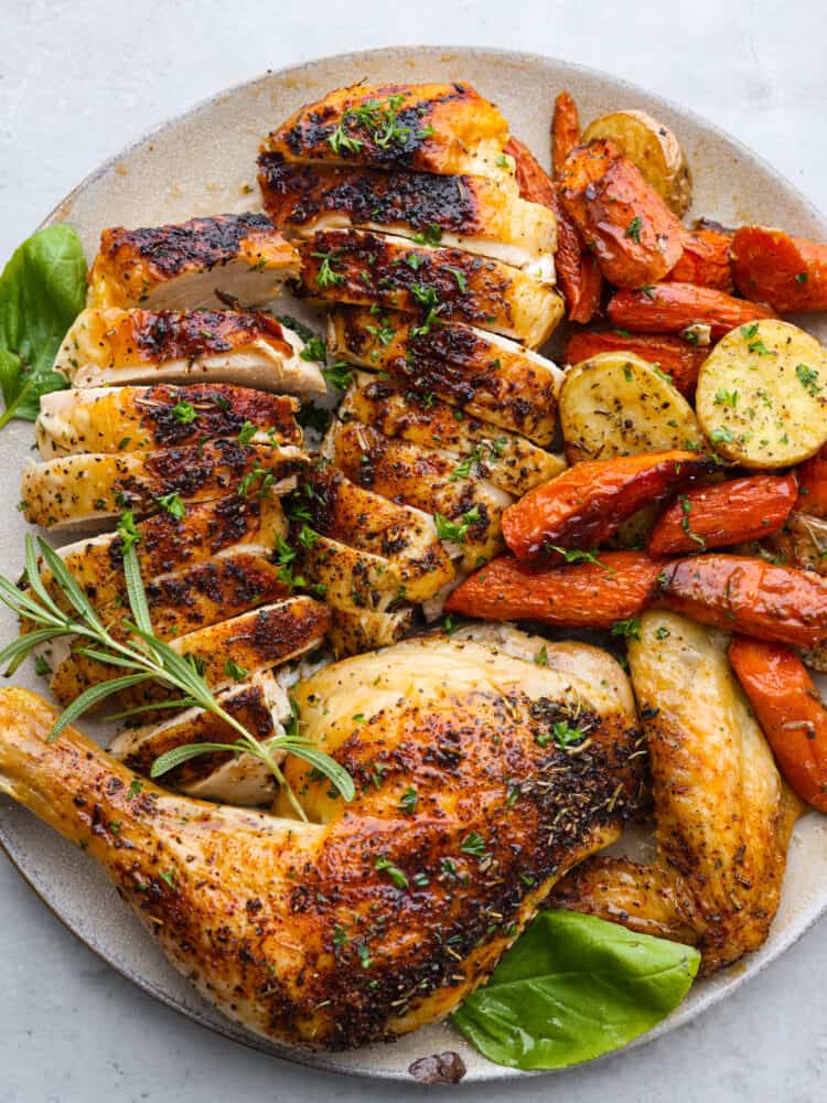 Spatchcock chicken is the secret to the most tender chicken and this method locks in all the juicy flavors. Seasoned with a delicious rub and oven-roasted to perfection this will be your new favorite way of cooking a chicken. Close up view of spatchcock chicken carved and served on a platter with roasted carrots, potatoes, and fresh herbs.
