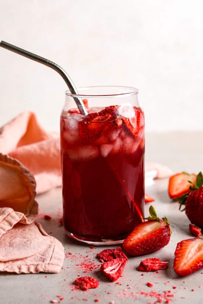 This Strawberry Acai Refresher is a refreshing drink that's sure to help you beat the heat! Whether you're lounging by the pool, hosting a summer soirรฉe, or simply in need of a tropical escape, this refresher will be your go-to beverage. A strawberry acai refresher in a clear glass cup with a metal straw.