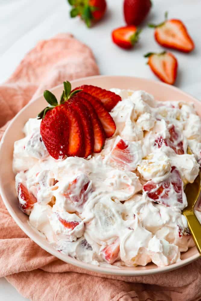 Strawberry Cheesecake Salad is a sweet and creamy dessert with fresh strawberries hidden throughout. This is the biggest hit at any potluck and SO easy to make! Hero image of strawberry cheesecake salad in a peach-colored bowl.