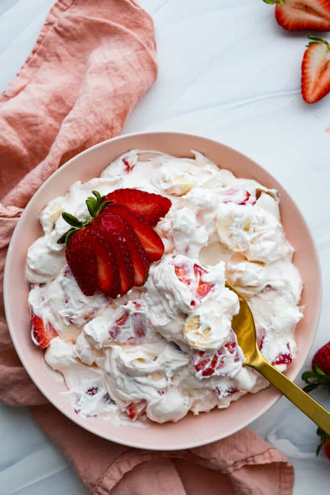 Strawberry Cheesecake Salad is a sweet and creamy dessert with fresh strawberries hidden throughout. This is the biggest hit at any potluck and SO easy to make! Top-down view of creamy strawberry salad.