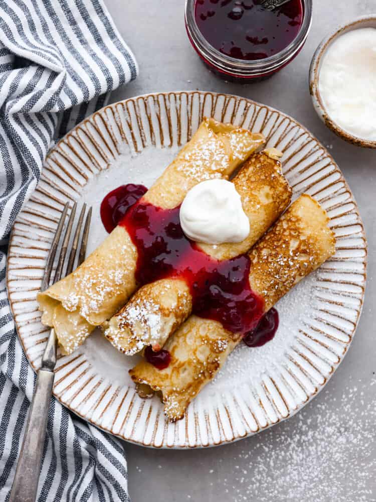 Homemade Swedish pancakes are the ultimate breakfast treat! They're soft, tender, and even better when topped with fresh whipped cream and lingonberry jam. Top-down view of pancakes served with lingonberry sauce and whipped cream on a gray plate.