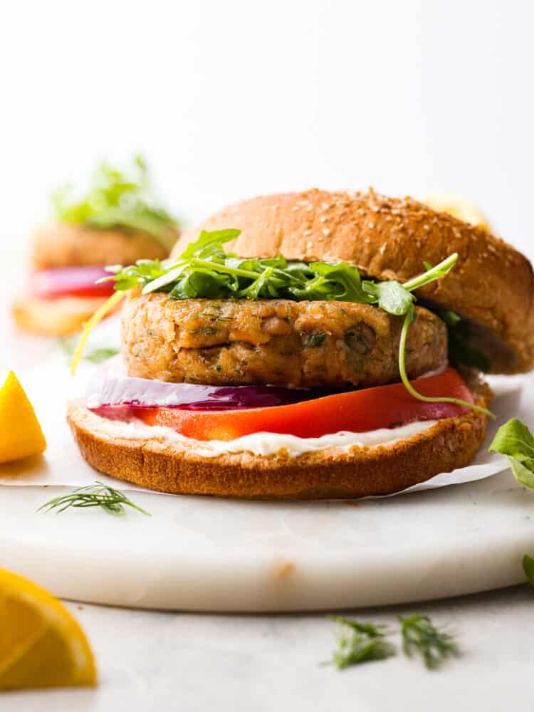 Tuna burgers are like a tasty remix of regular beef burgers, bringing a lighter and more flavorful option to the table that seafood fans can't resist. With zingy lemon, fragrant herbs, and the deliciousness of tuna, these burgers are a total mouthwatering delight that will satisfy even the biggest burger cravings. Hero image of a tuna burger topped with tomato and greens.