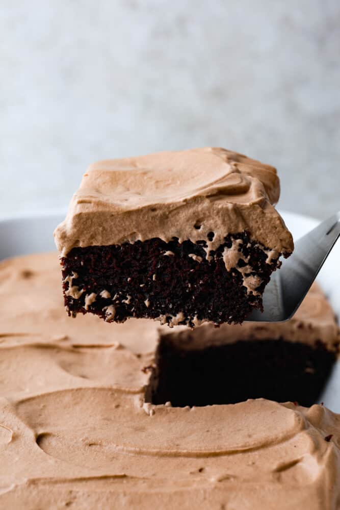 If you're looking for a fun and delicious dessert then you have to try this Wacky Cake recipe! This cake is full of rich chocolate flavor and topped with easy-to make chocolate whipped cream. A slice of wacky cake being removed from the pan with a cake server.
