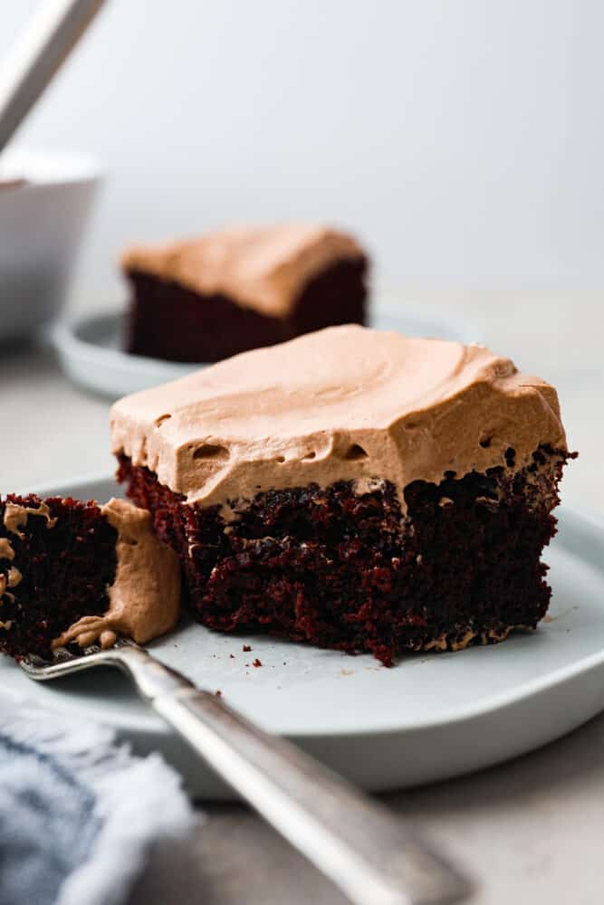 If you're looking for a fun and delicious dessert then you have to try this Wacky Cake recipe! This cake is full of rich chocolate flavor and topped with easy-to make chocolate whipped cream. A slice of wacky cake on a plate with a fork and a bite take out.