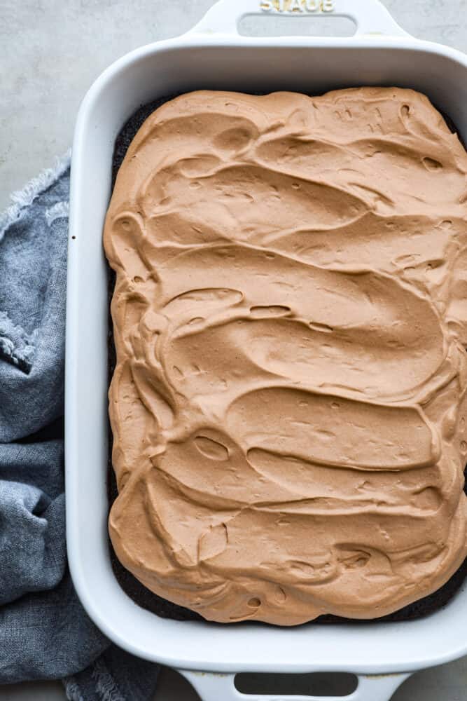 If you're looking for a fun and delicious dessert then you have to try this Wacky Cake recipe! This cake is full of rich chocolate flavor and topped with easy-to make chocolate whipped cream. The top view of wacky cake all frosted and in the 9x13 pan.