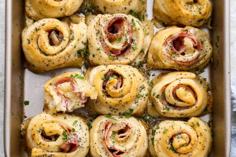Hot Ham and Swiss Pinwheels have smoked ham and melty swiss cheese that are rolled up in croissantย dough and are brushed with a buttery garlic poppyseed topping! The perfect insanely delicious quick and easy dinner or appetizer! The top view of a pan with pinwheels.
